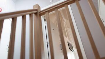 A wooden staircase with a handrail leading to a room with a door and a light switch on the wall.
