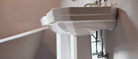 Un baño con lavamanos pedestal blanco, una bañera y un espejo en la pared.