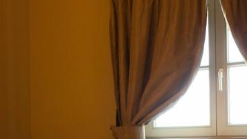 A room with a bed, a window with curtains, a radiator, and wooden flooring.