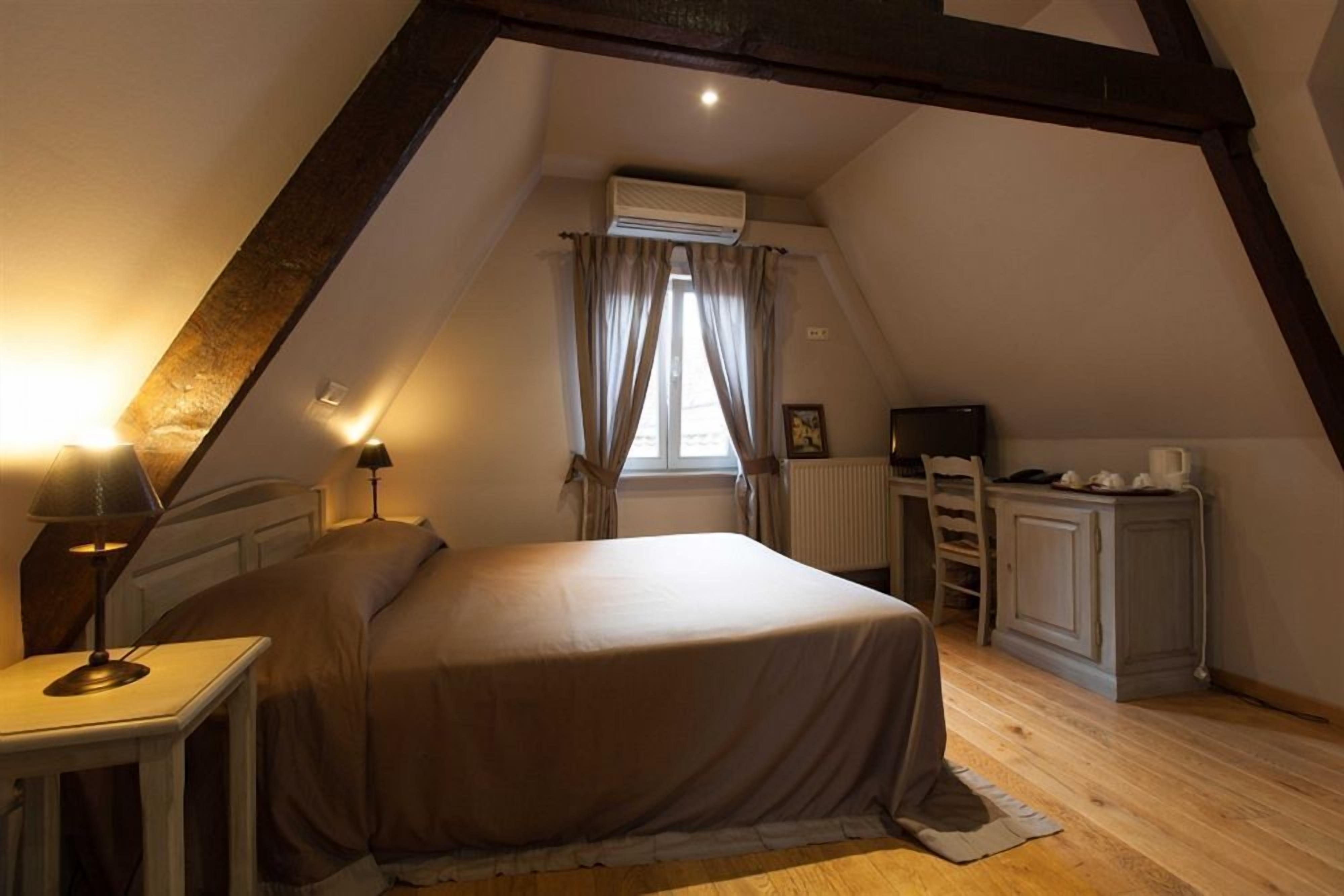 A bedroom with a bed, bedside table, lamp, and a window with curtains.
