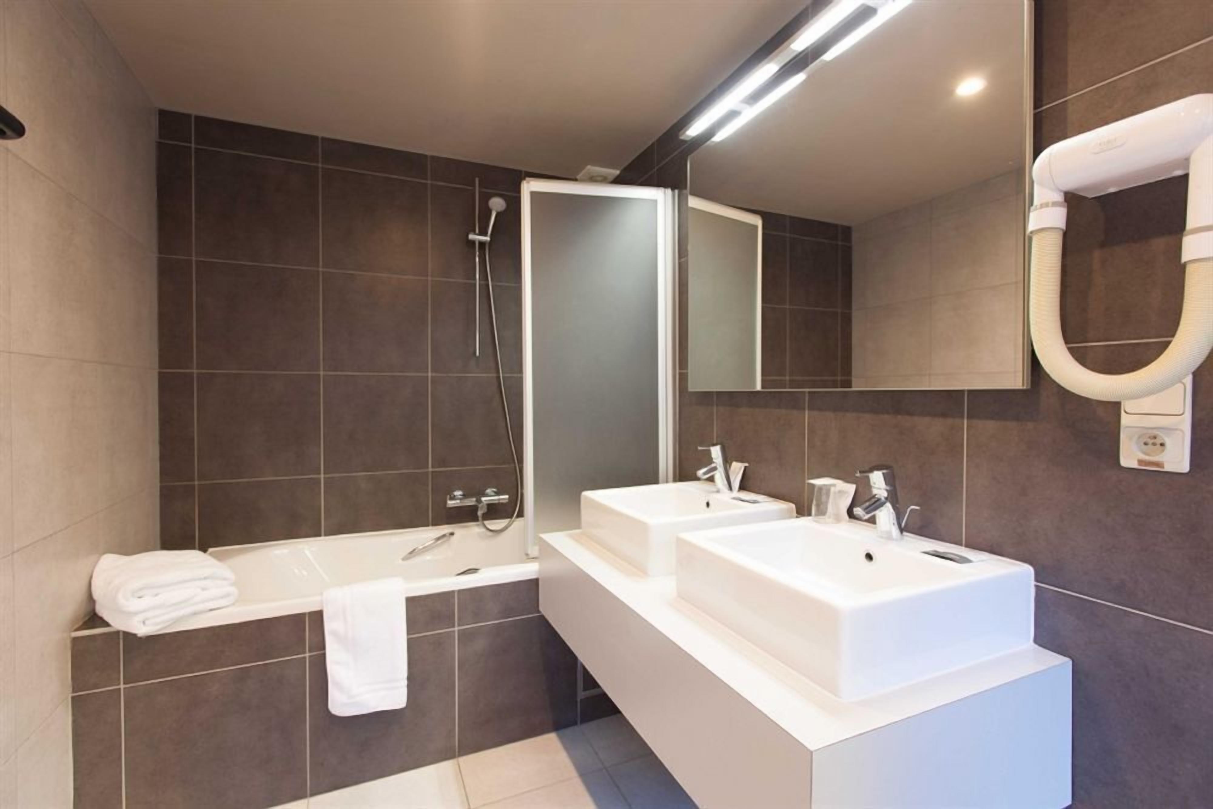 A modern bathroom with two sinks, a bathtub, and a large mirror.