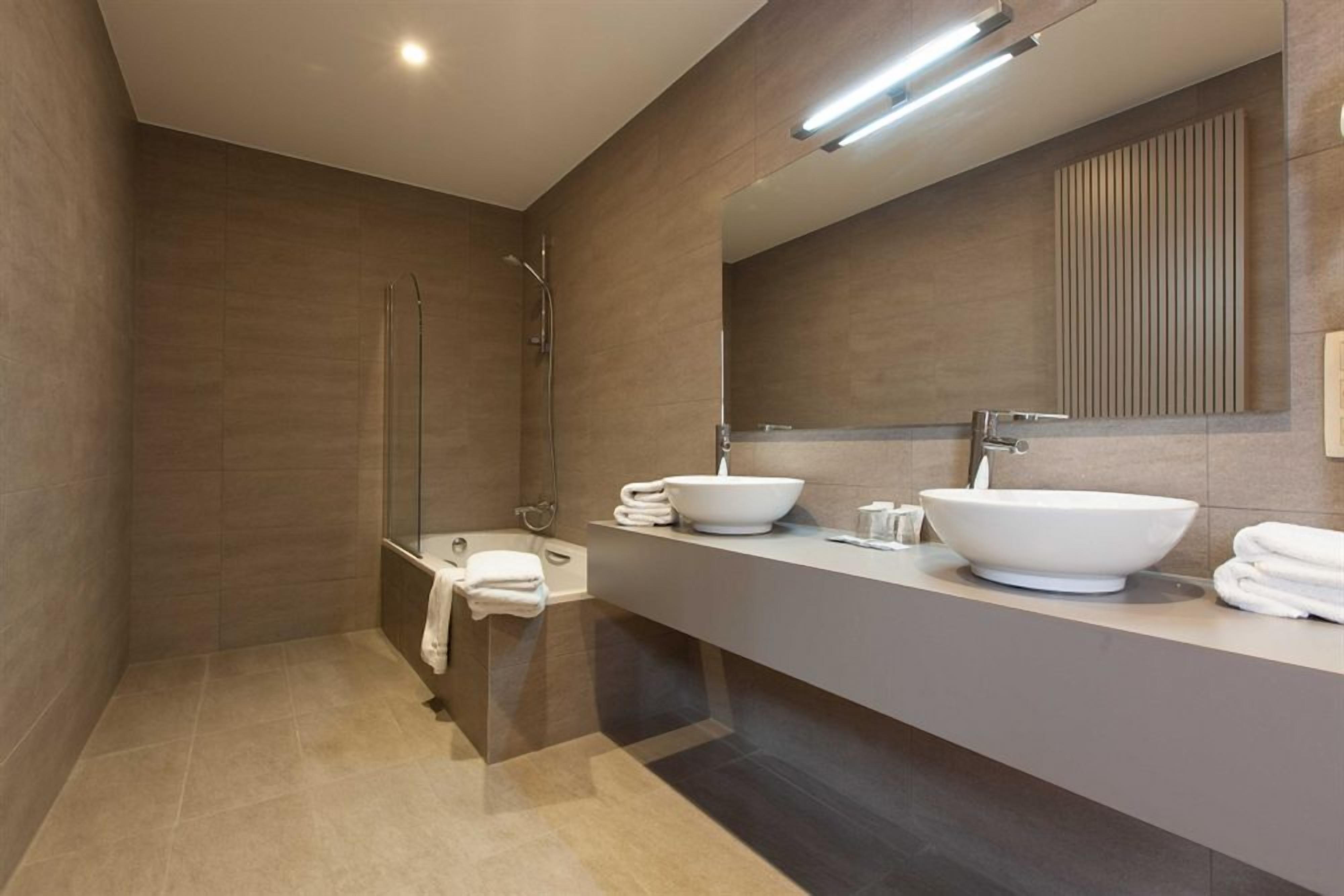 A modern bathroom with a walk-in shower, a large vanity with two sinks, and a mirror above the vanity.