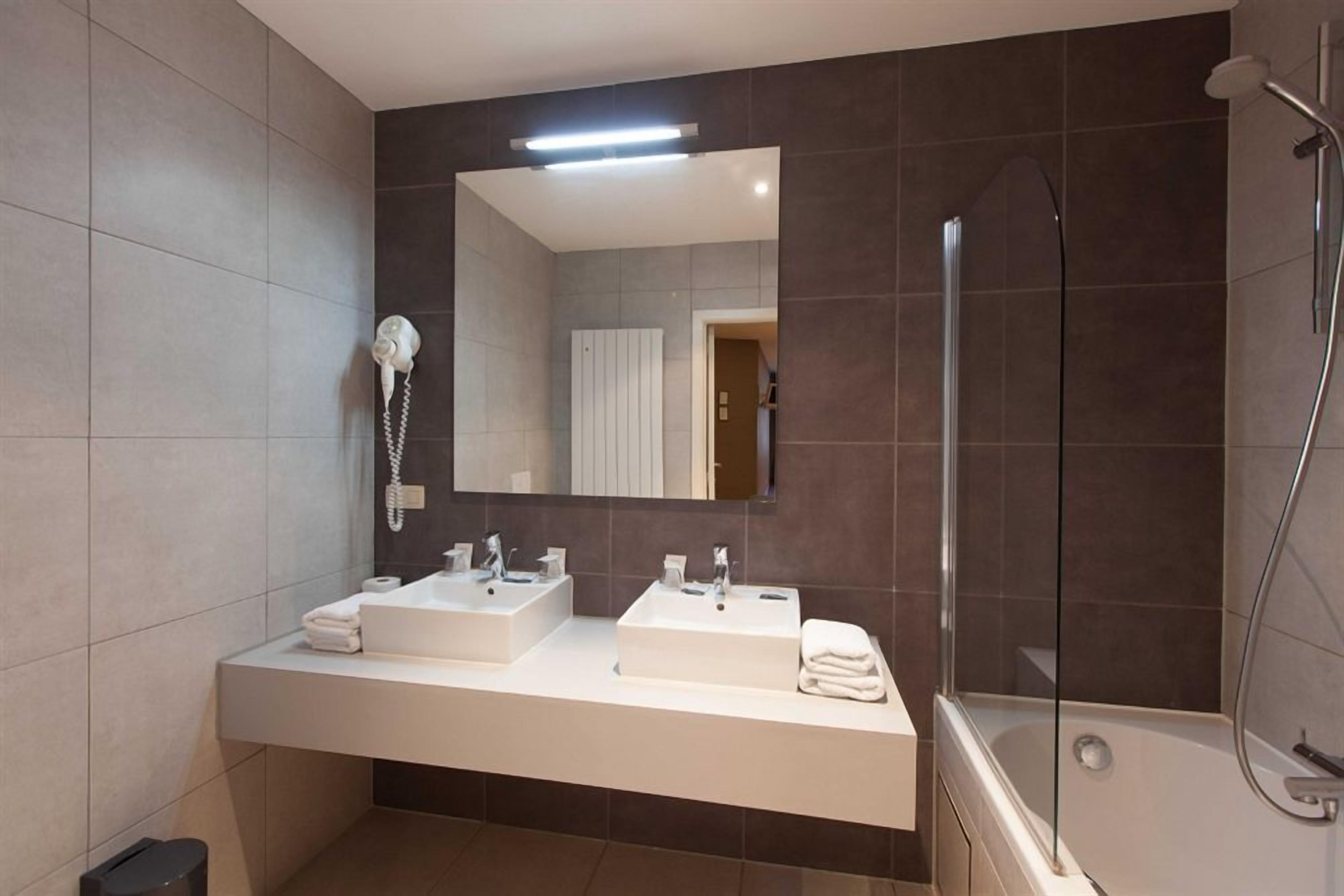 A modern bathroom with two sinks, a large mirror, a hairdryer, and a glass-enclosed shower.