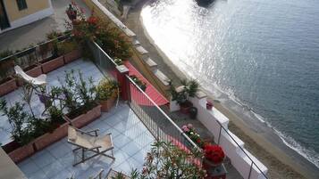 A balcony with potted plants and outdoor furniture overlooking a beach.