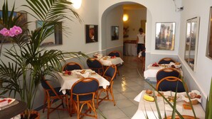 Un comedor con mesas dispuestas para comer, sillas, plantas en macetas y obras de arte en las paredes.