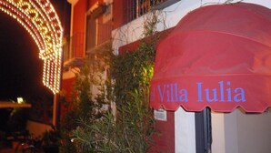 Villa Julia con un toldo rojo y un letrero, rodeada de vegetación y una estructura de iluminación decorativa.