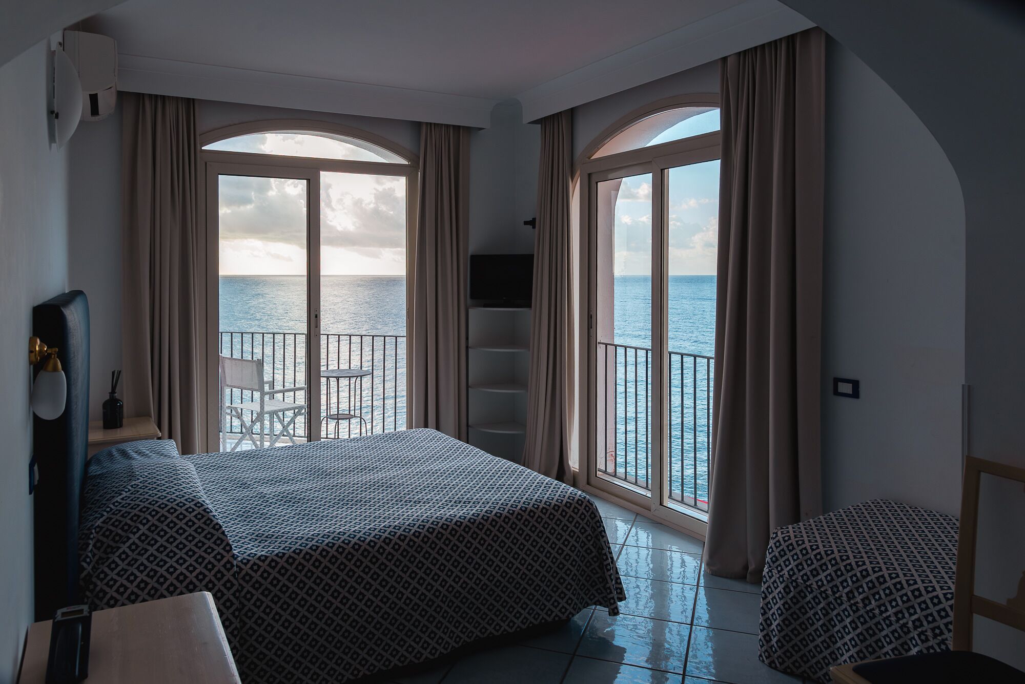 Una camera d'albergo con un letto, una sedia, un tavolino e un balcone vista mare.