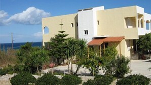 A modern two-story building with a flat roof, a small attached structure with a tiled roof, and a clear view of the ocean. - Hotel Babis (Rethymno)
