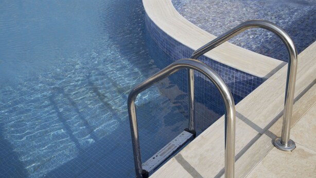 A swimming pool with clear blue water and a metal ladder leading into it. - Hotel Babis (Rethymno)