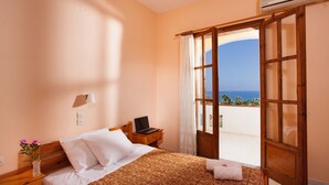 A bedroom with a bed, a nightstand, a lamp, and a view of the sea through an open door. - Hotel Babis (Rethymno)