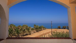 A view through an arched window overlooking a beach with palm trees and a clear blue sky. - Hotel Babis (Rethymno)