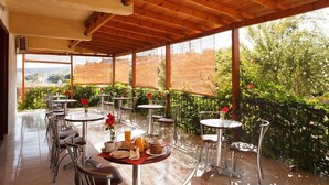 An outdoor café with tables and chairs, surrounded by greenery and a wooden pergola. - Hotel Babis (Rethymno)