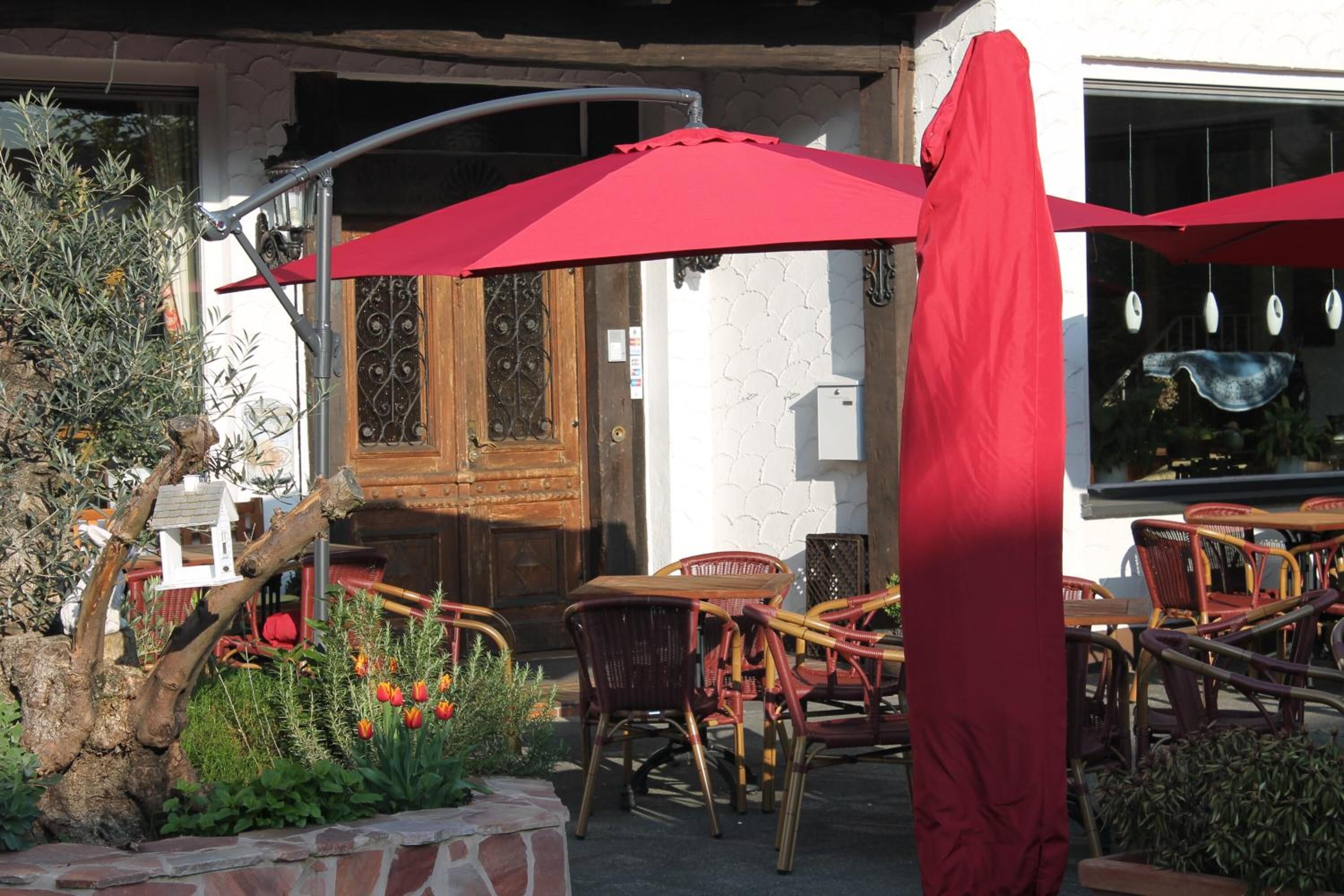An outdoor seating area with red umbrellas, wicker chairs, and a rustic wooden door.