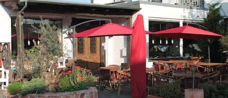 Een terras met stenen plantenbakken, houten stoelen en rode parasols.