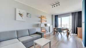 Ett modernt vardagsrum med en grå soffa, ett vitt soffbord, en matplats med ett träbord och stolar samt ett stort fönster med gardiner.