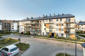 Un immeuble résidentiel à plusieurs étages, doté de balcons, d’une allée pavée et d’un petit espace de stationnement.