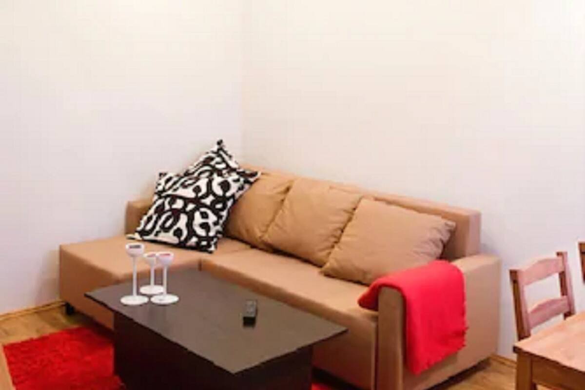 Uma sala de estar aconchegante com um sofá bege, um tapete vermelho e uma mesa de centro de madeira.