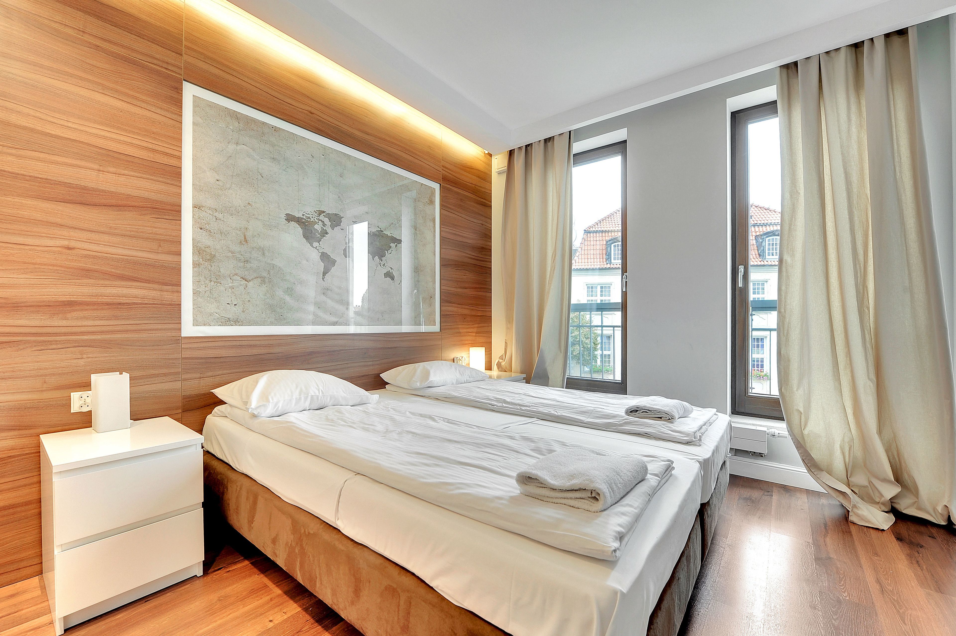 Habitación de hotel moderna con dos camas, cabecero de madera, un cuadro abstracto grande y una ventana con cortinas.