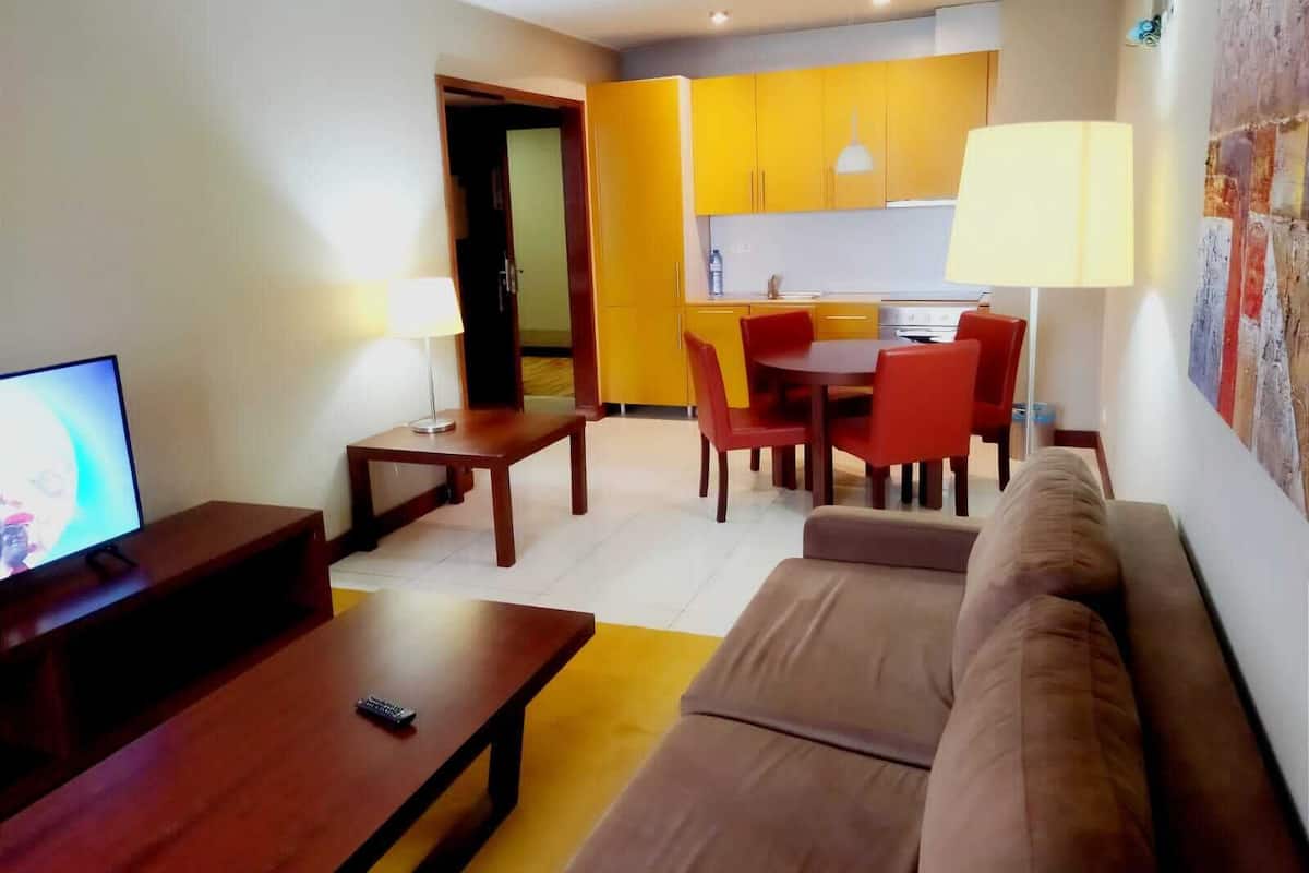 A living room with a TV, a sofa, a coffee table, and a dining area with chairs and a table.