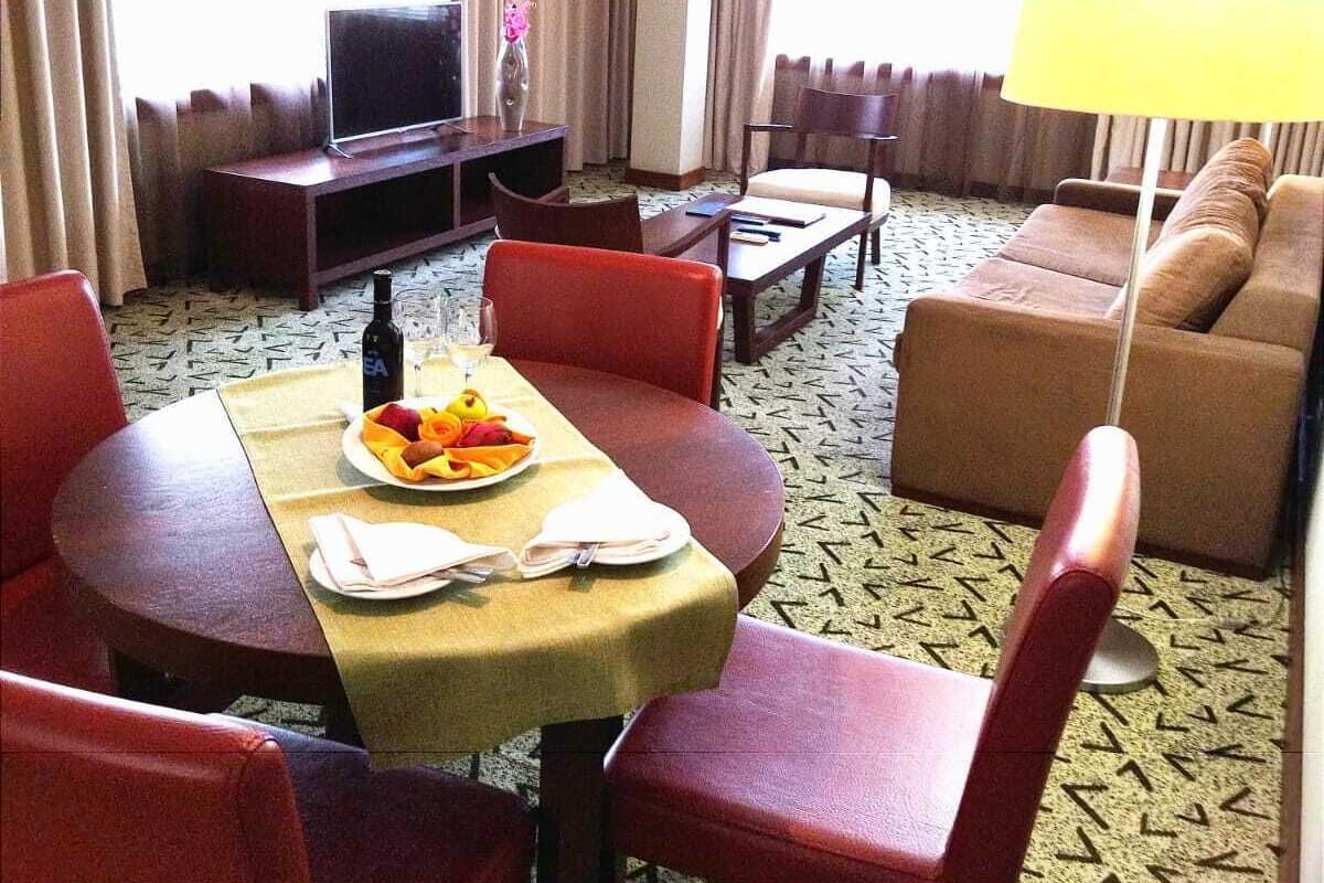 A hotel room with a dining area, a sofa, a TV, and a lamp.