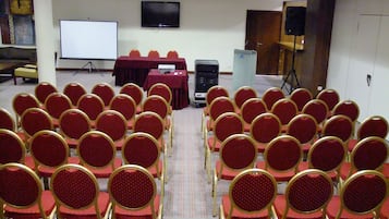 Une salle de conférence avec des rangées de chaises rouges et un tableau blanc.