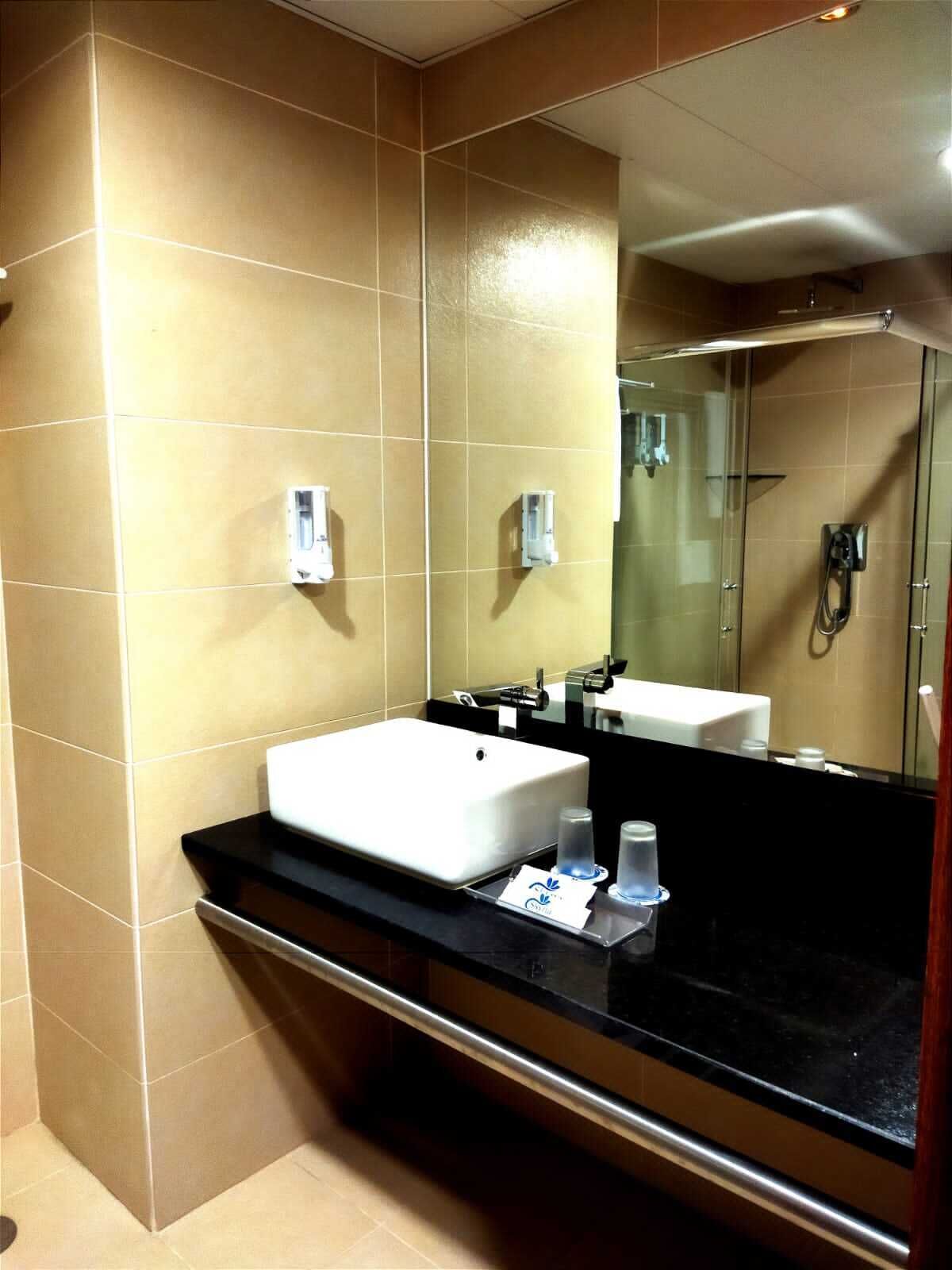 A modern bathroom with a large mirror, a white sink, and a glass-enclosed shower.