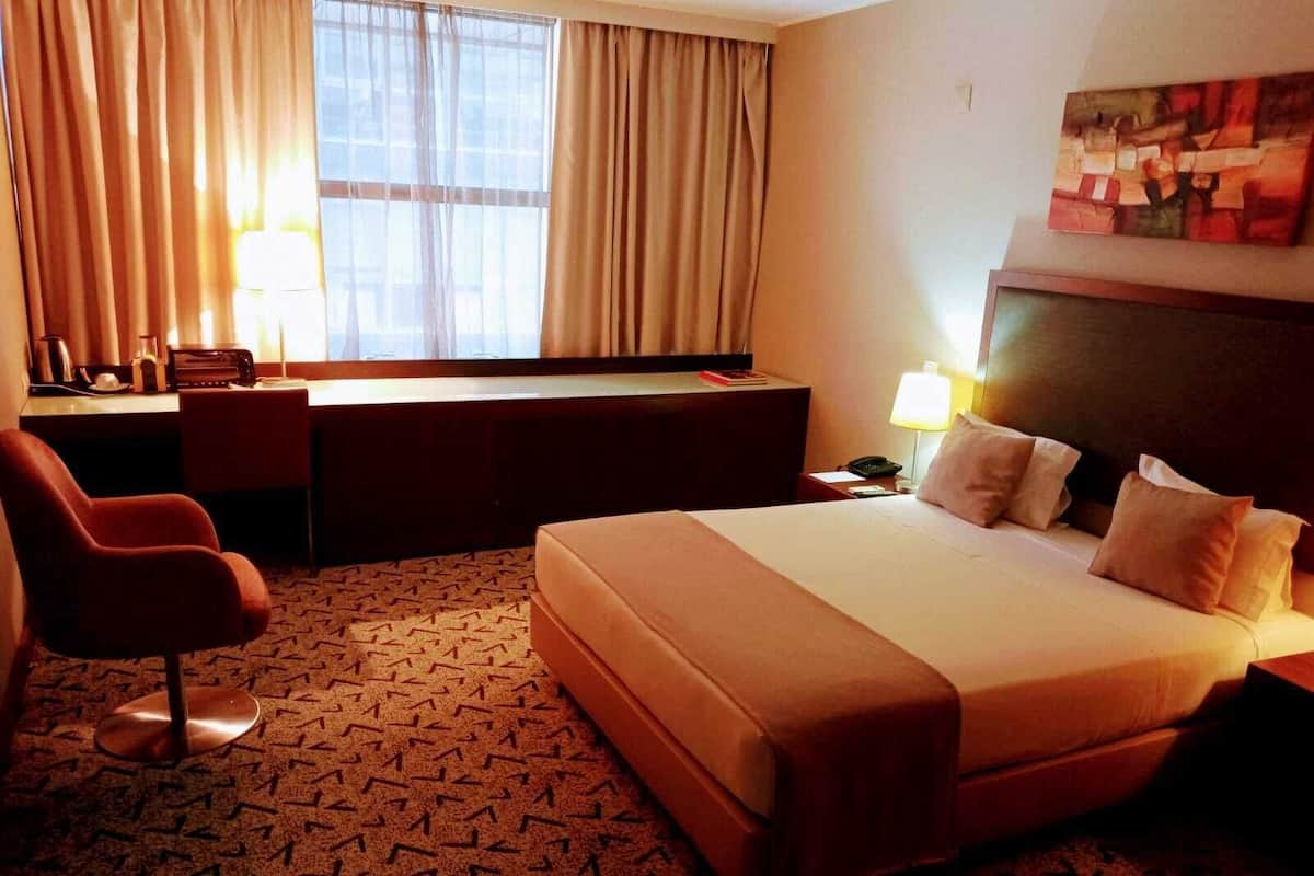A hotel room with a large bed, a desk, a chair, and a window with curtains.
