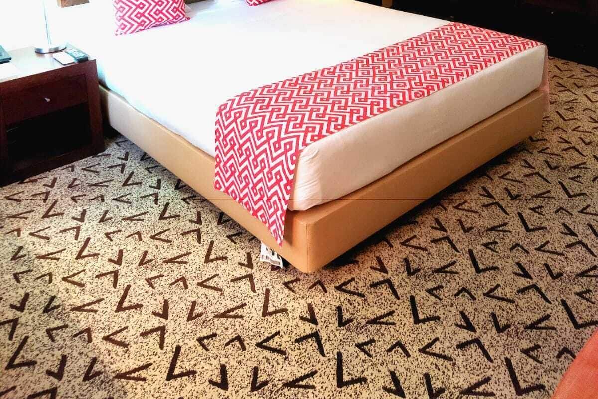 A hotel room with a large bed, a headboard, a bedside table with a lamp, a wall-mounted artwork, and a wardrobe.