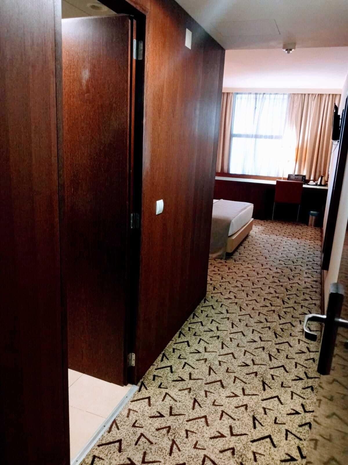 Une chambre d’hôtel avec une armoire en bois, un lit, un bureau et une fenêtre avec des rideaux.