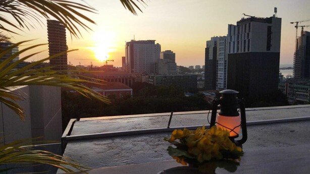 A cityscape at sunset with modern buildings, a balcony with a flower arrangement, and a lantern. - Skyna Hotel Luanda (Luanda)