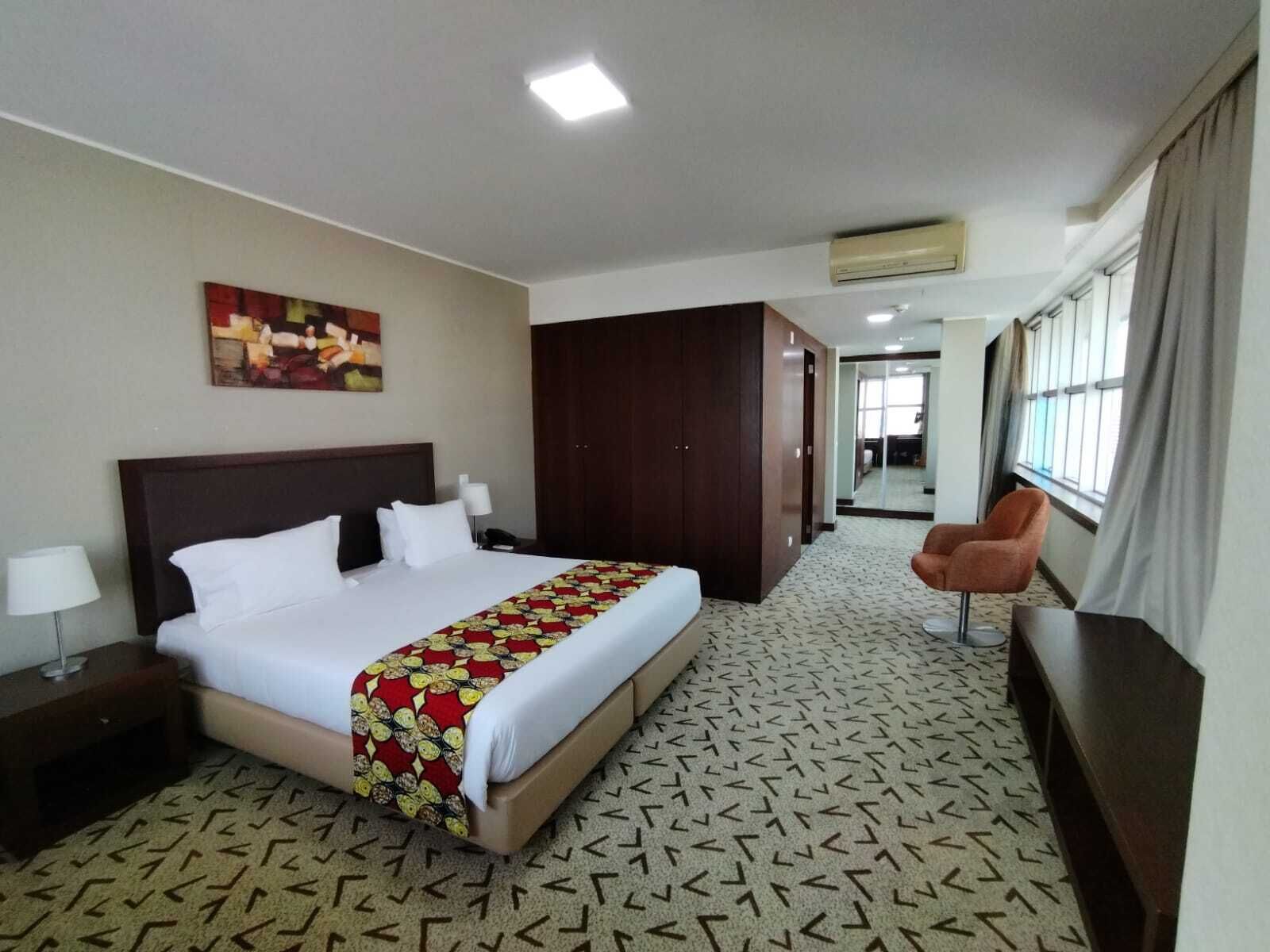 A hotel room with a bed, a desk, a chair, a wardrobe, and a painting on the wall.