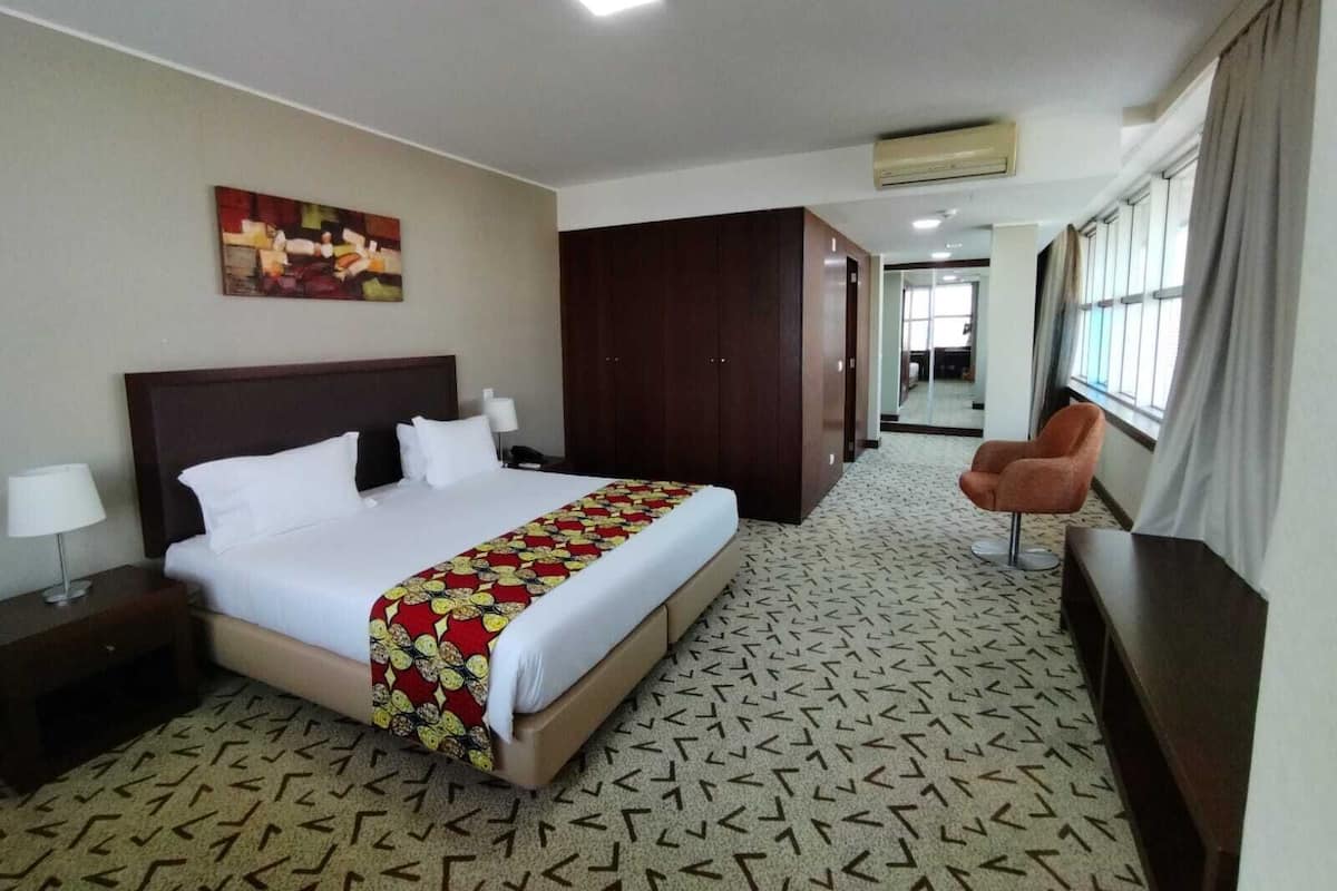 A hotel room with a bed, a desk, a chair, a wardrobe, and a painting on the wall.