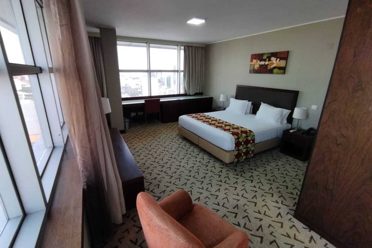 A hotel room with a bed, desk, chair, and large windows.