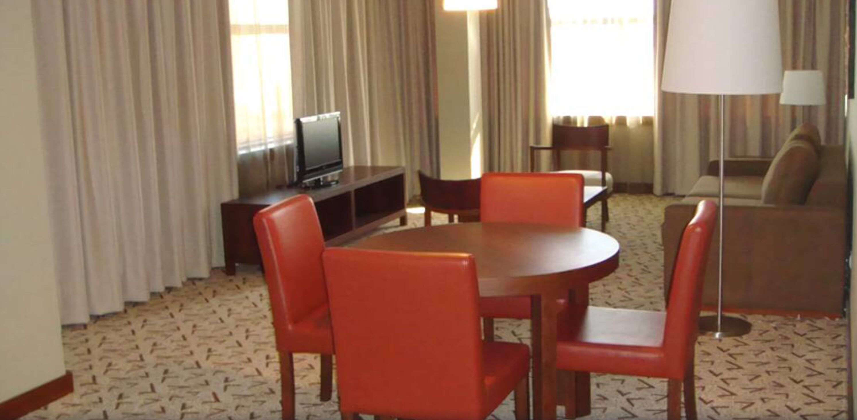 A hotel room with a dining area featuring a round table and four chairs, a television on a stand, and a sofa.