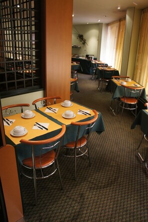 A hotel dining area with multiple tables, chairs, and a buffet setup in the background. - Hotel Toulouse Aéroport (Toulouse)