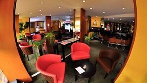 Un hall de hotel con sillas rojas y marrones, una mesita y una planta en maceta.