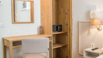 Een hotelkamer met een houten bureau, een stoel, een bed, een kledingkast, een spiegel, een lamp en een telefoon.