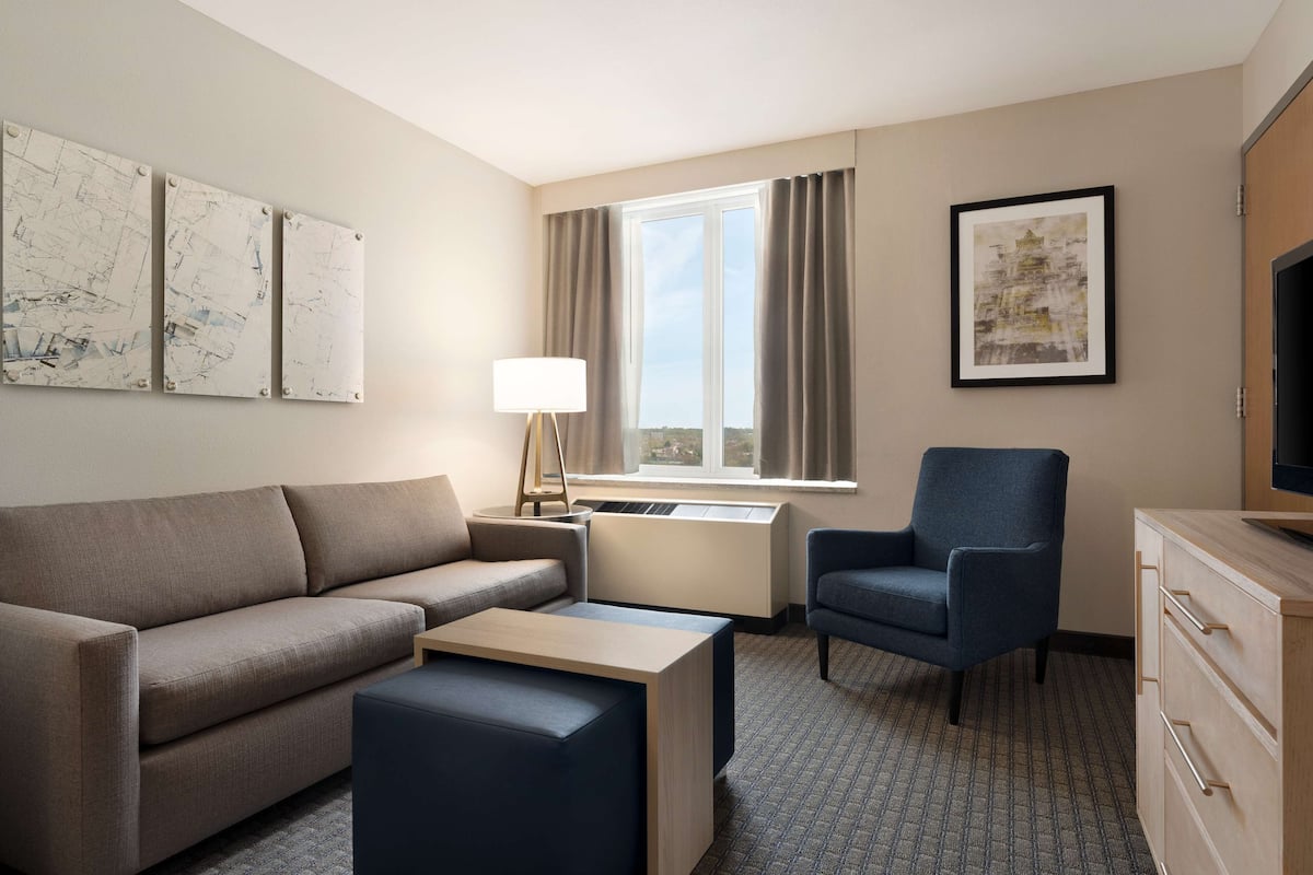 Une chambre d’hôtel équipée d’un canapé, d’une petite table, d’une chaise, d’un bureau, d’une lampe, d’une télévision et d’œuvres d’art accrochées aux murs.