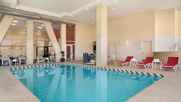 An indoor swimming pool with tiled flooring, lounge chairs, and a seating area with tables and chairs.