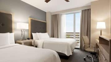 A hotel room with two beds, a desk, a chair, a lamp, and a large window with curtains.