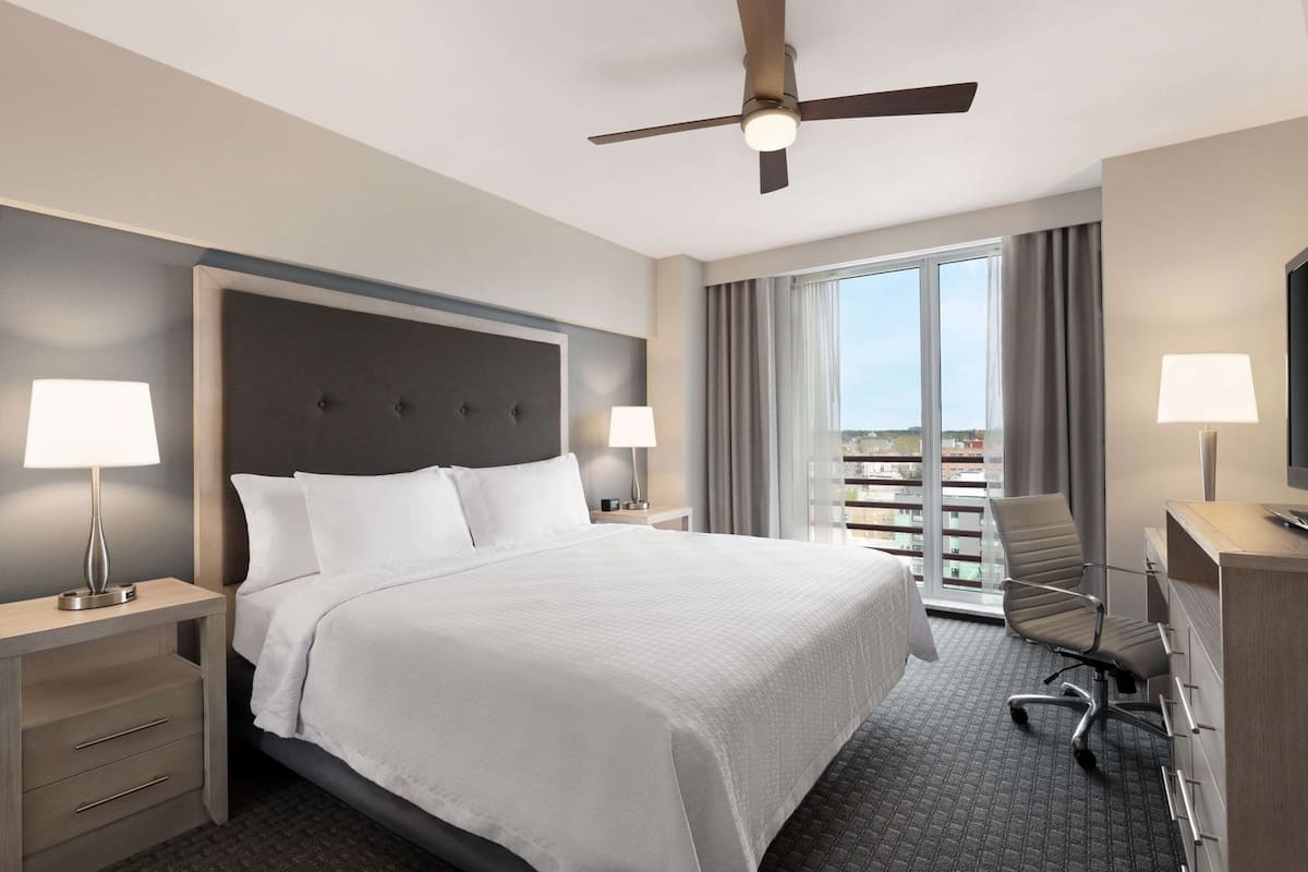 Une chambre d’hôtel équipée d’un lit, d’un bureau, d’une chaise, d’un ventilateur de plafond et d’une grande fenêtre.