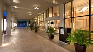 Un pasillo de hotel con puertas de vidrio, plantas en macetas y un mostrador de recepción.