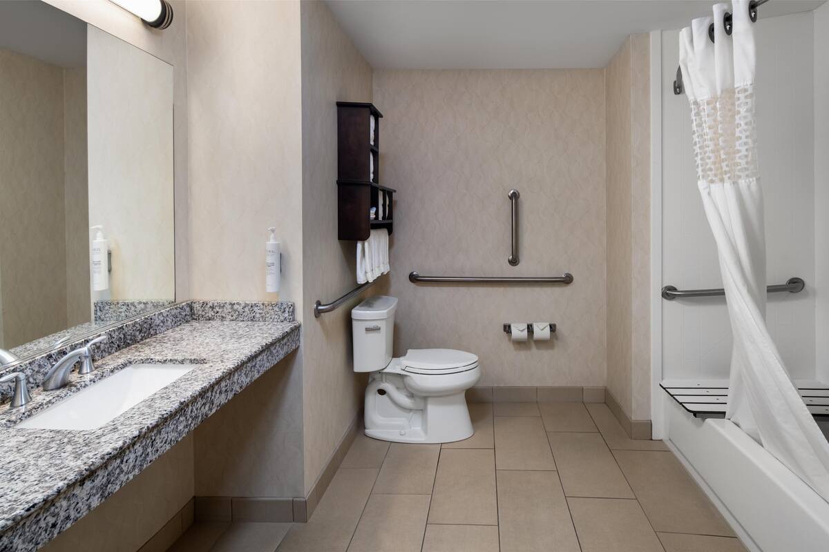 A modern bathroom with a granite countertop sink, a white toilet, a shower with a white curtain, and a grab bar.