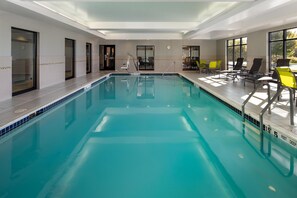 A large indoor swimming pool with clear water, surrounded by lounge chairs and a sunlit area with large windows.