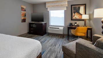 A hotel room with a bed, a desk with a chair, a television, a window with a view, and artwork on the walls.