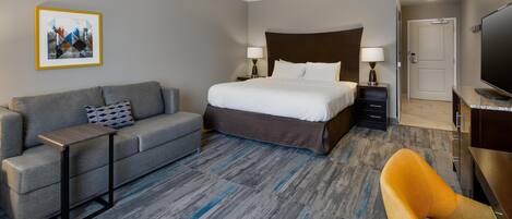 Una habitación de hotel con una cama, un sofá, una mesita, un televisor y una puerta.