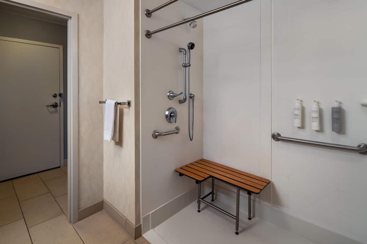 A modern bathroom with a shower, a bench, and handrails.
