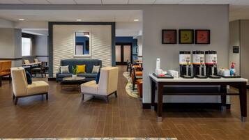 A modern hotel lobby with seating areas, a coffee station, and framed artwork on the wall.