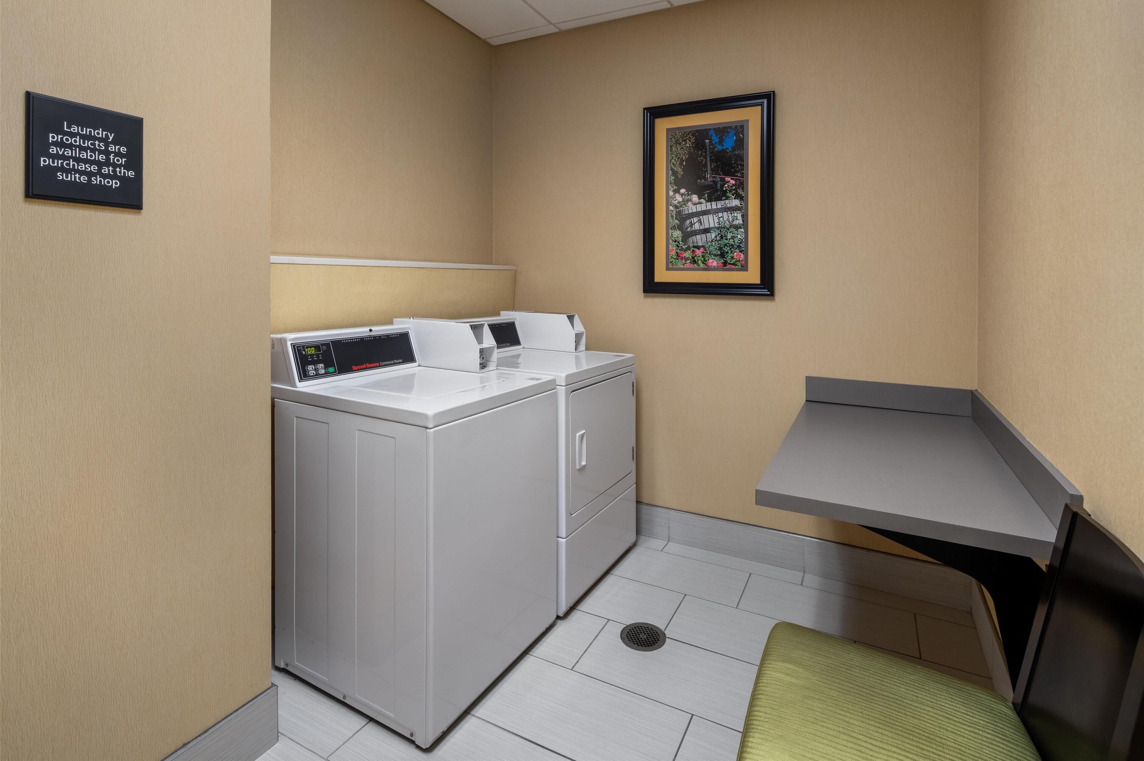 A laundry room with a washing machine and dryer, a small table, and a framed picture on the wall.