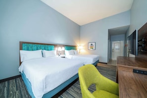 A hotel room with two beds, a desk, a chair, and a TV.